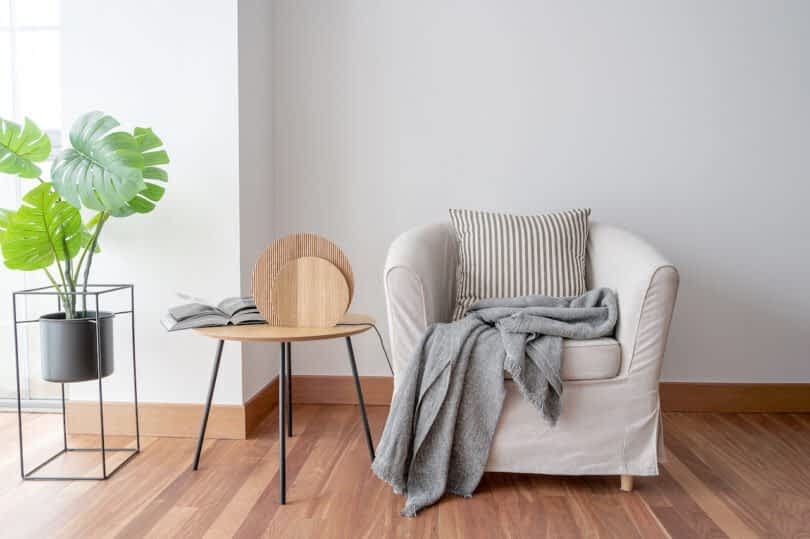A cozy armchair with a striped cushion and gray throw blanket is next to a small wooden table with a lamp and open book