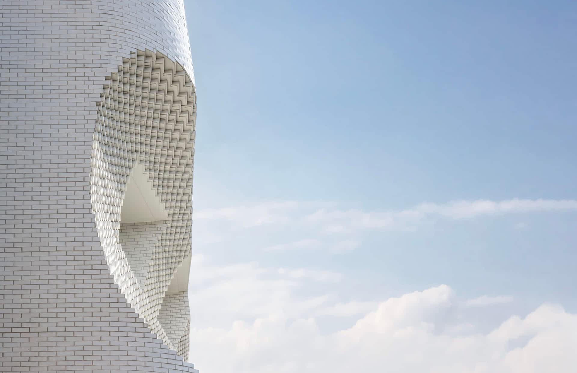 a detail of a concave form in a white brick facade, set against a blue sky