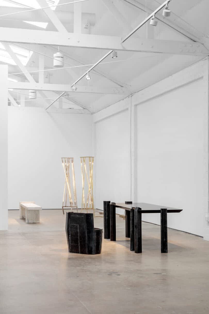 An art gallery with contemporary furniture and light installations in a minimalist white space with high ceilings and exposed beams, featuring pieces by Vincenzo De Cotiis.