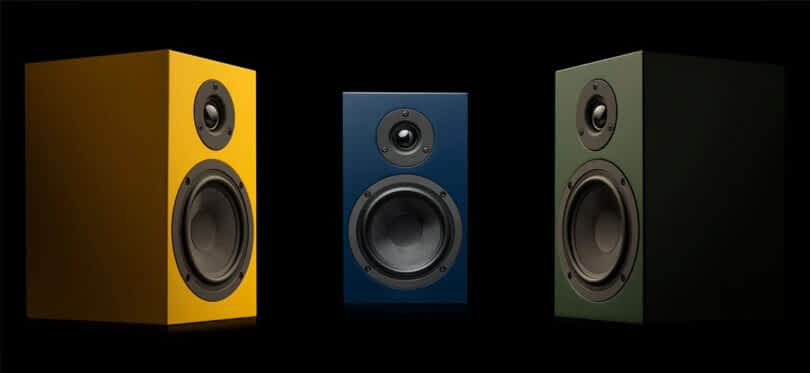 Three Pro-Ject Speaker Box 5 S2 in yellow, blue and green angled toward one another set in a black background.