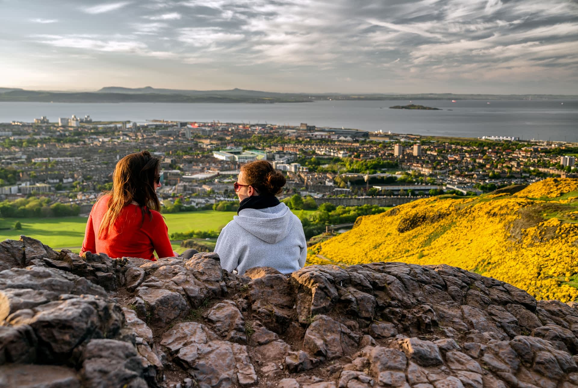 Arthur's Seat offers stunning views over Edinburgh. Girls sitting on the hill of Arthur's Seat overlooking Edinburgh.