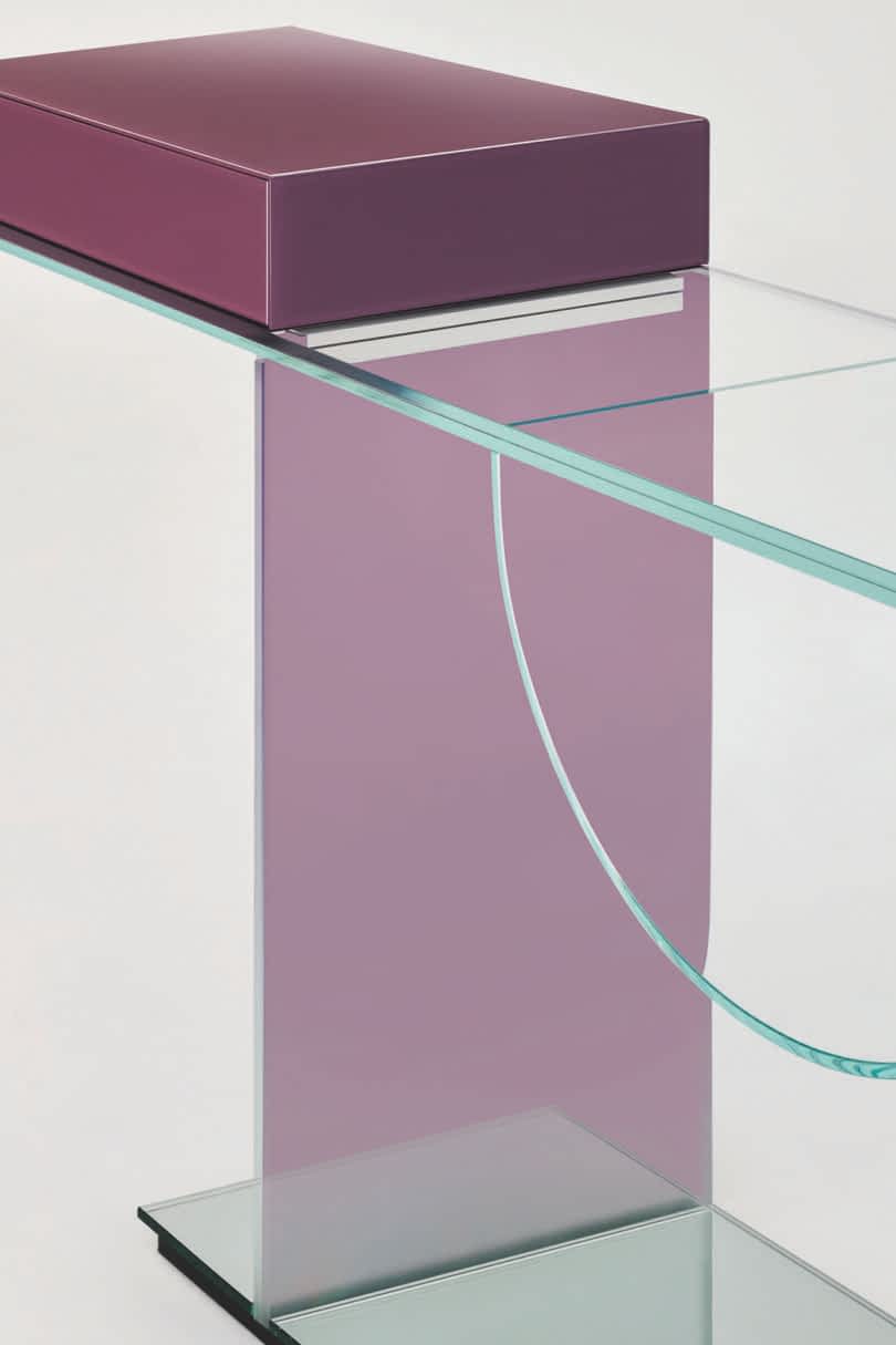 Detail of a modern glass console featuring a purple rectangular top, a vertical support, and a curved glass shelf.