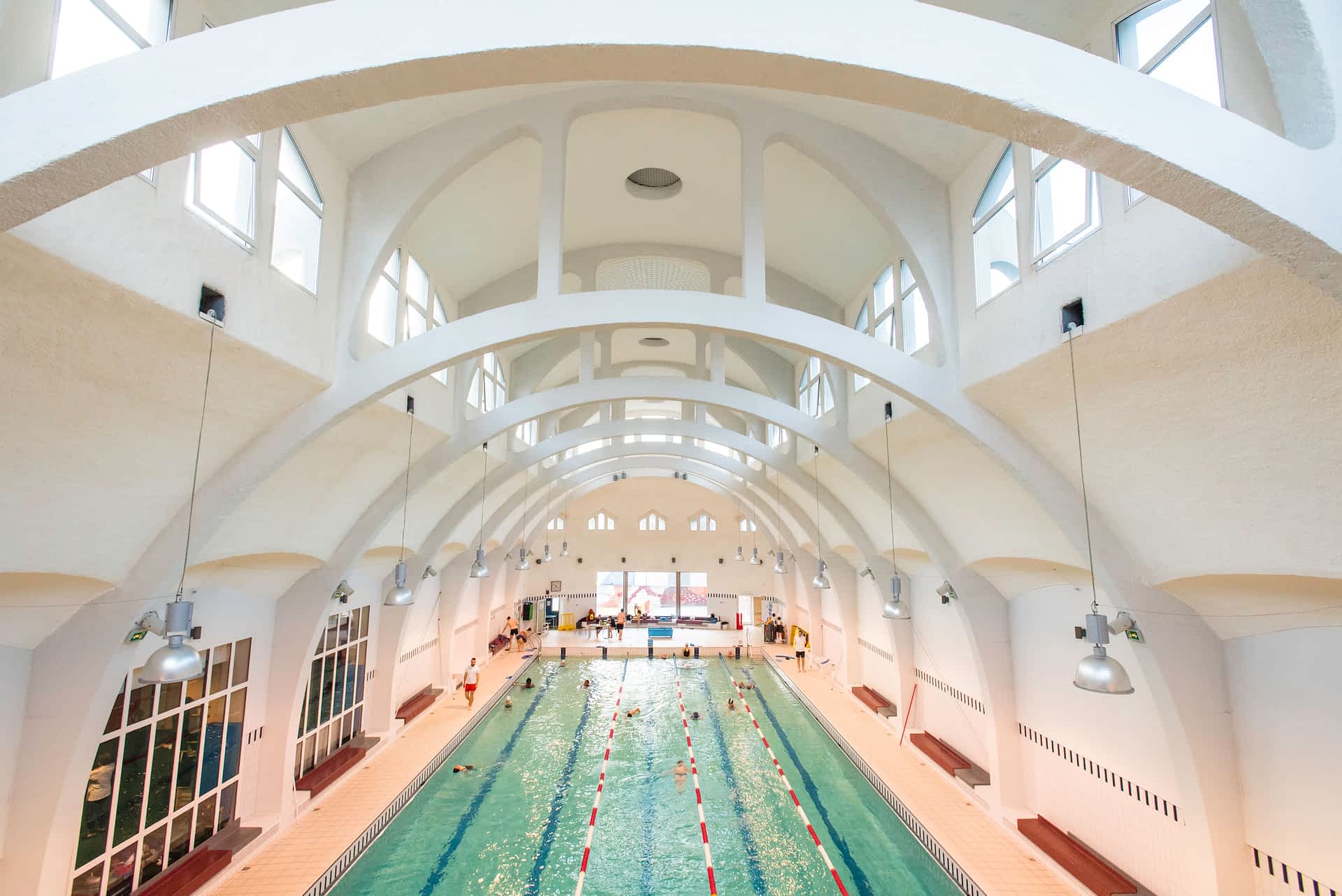 Swimmers swim back and forth in an indoor lap pool beneath white arched ceilings