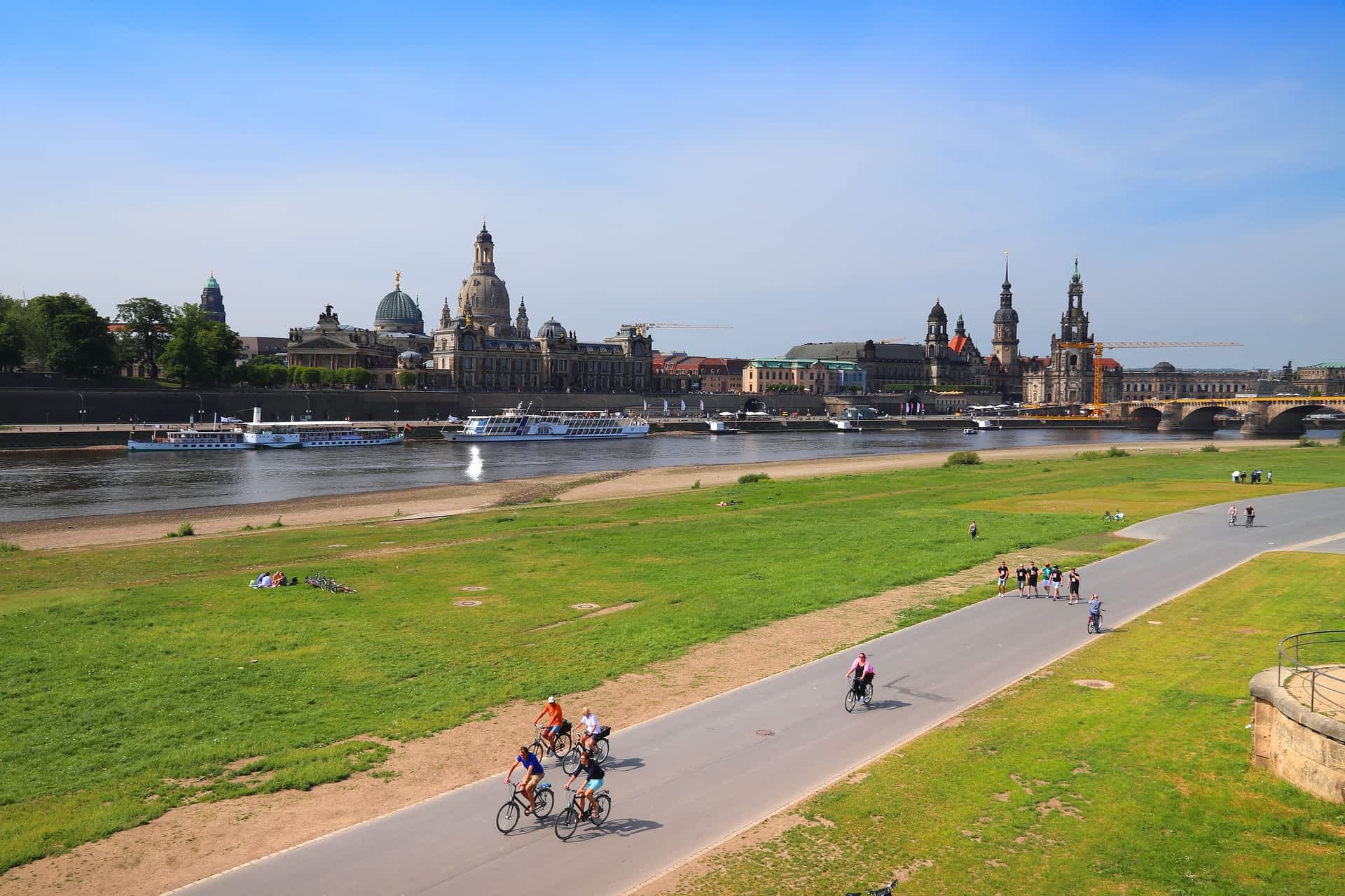 shutterstock2422585419.jpg Cyclists ride on a path beside a river. A city with spires and domes is across the river