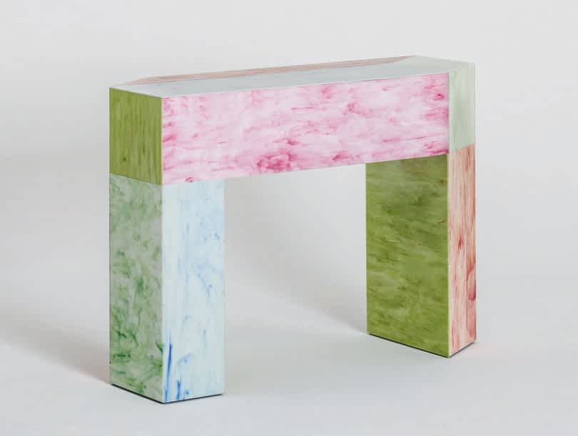 A multicolored geometric console featuring shades of pink, green, and purple with a marbled texture on a plain background.
