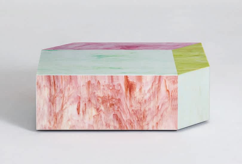 A multicolored geometric coffee table featuring shades of pink, green, and purple with a marbled texture on a plain background.