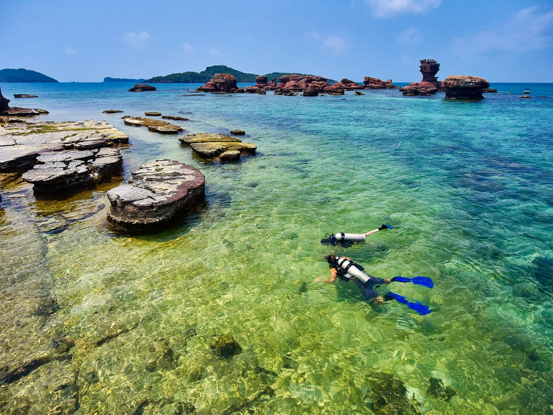 Two divers swim among rocks in clear water on Hom Gam Ghi in Phu Quoc