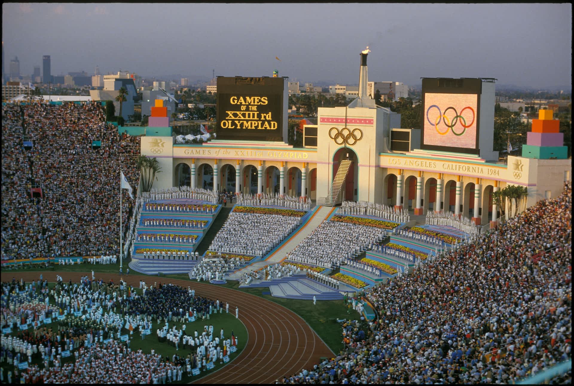 The opening ceremony of the 1984 Olympic Games, Los Angeles Memorial Coliseum, Los Angeles, California, USA Rafer Johnson lights the Olympic flame at the opening ceremony during the Olympic games in Los Angeles, CA. He is shown at the top of the steps, dressed in white, just below the Olympic rings.
