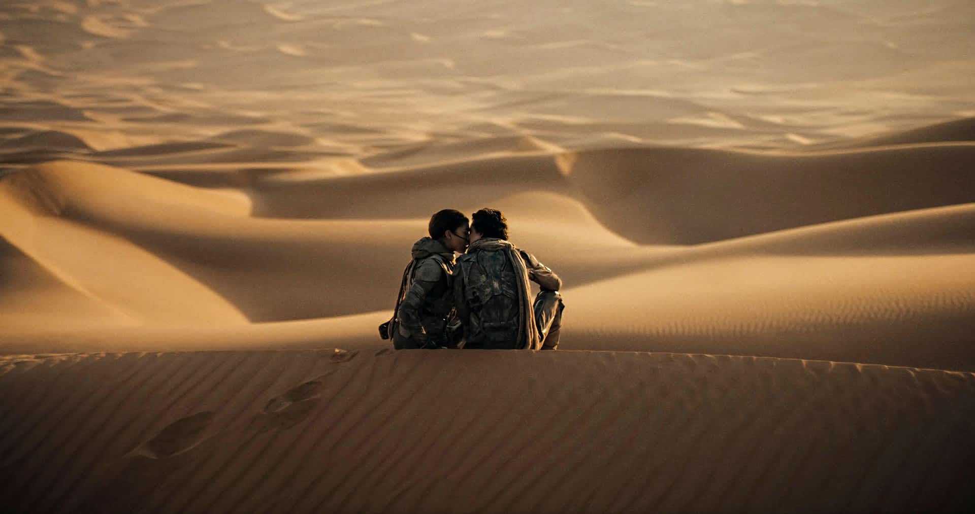 2WM2JP8-RM.jpg Two people sitting on sand dunes in a vast desert lean in to kiss