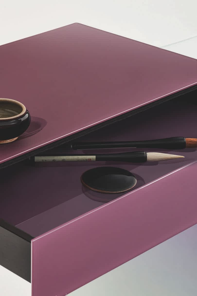 Detail of a modern glass console featuring a purple rectangular top, a vertical support, and a curved glass shelf.