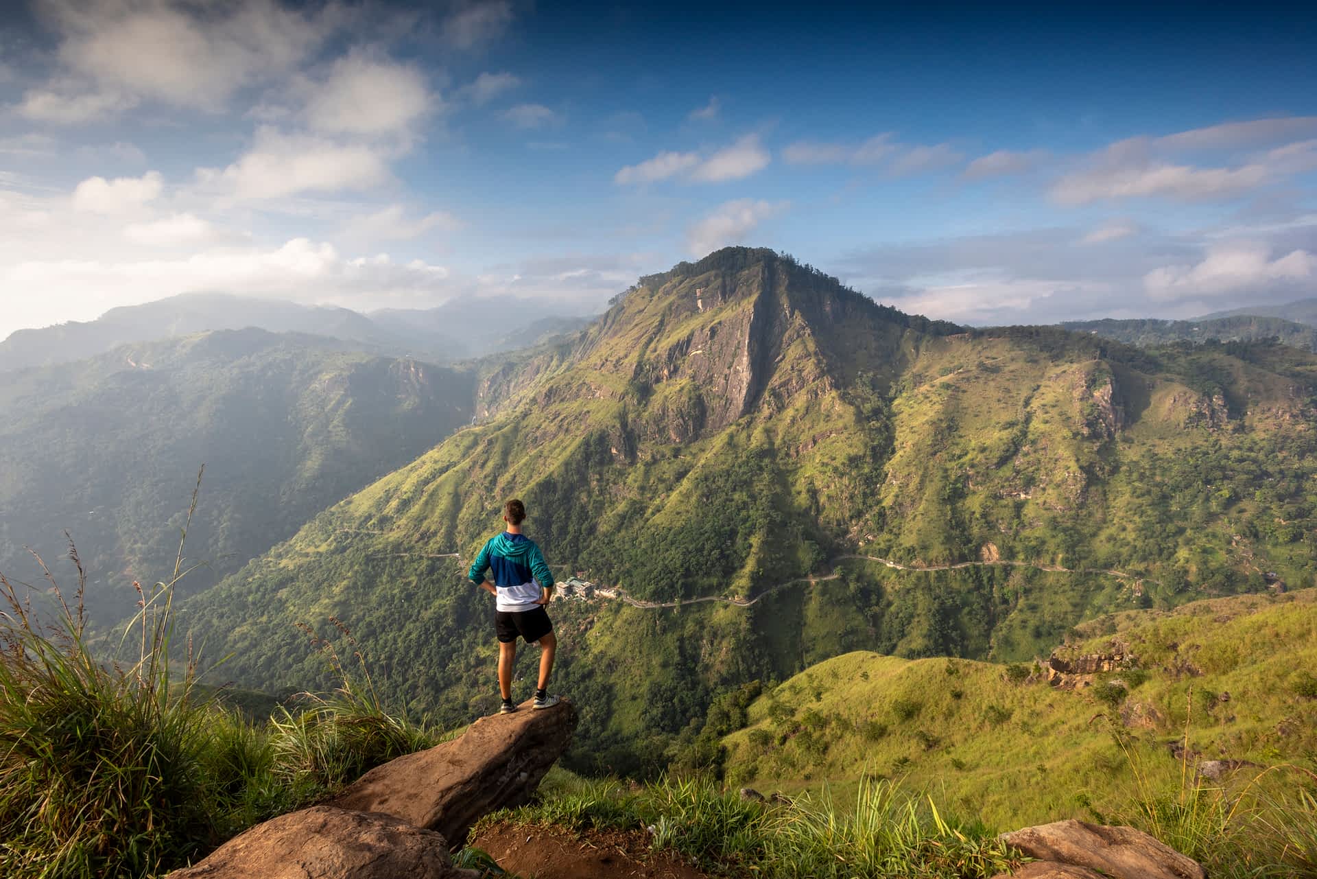 Little Adams Peak facing Ella Rock and the Ella Gap, Sri Lanka A man stands on a peak looking towards another distinctive hill in a lush green region