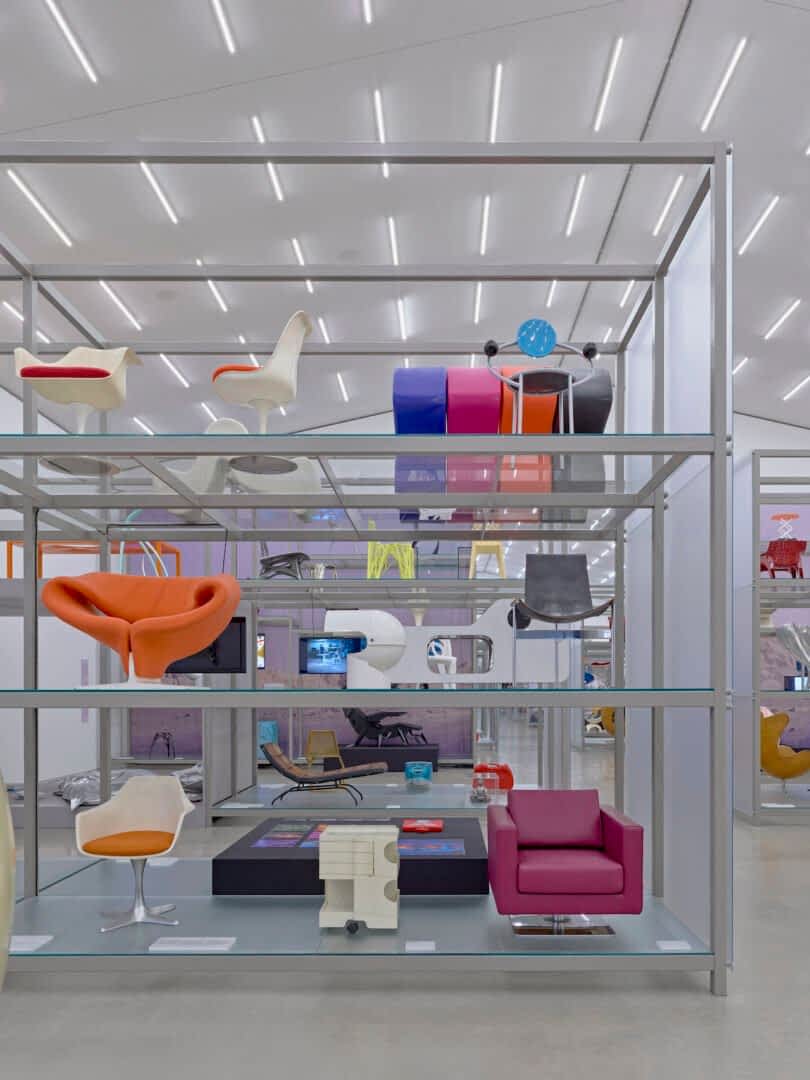 Shelves displaying various modern and colorful chairs in a well-lit exhibition space with a minimalist design