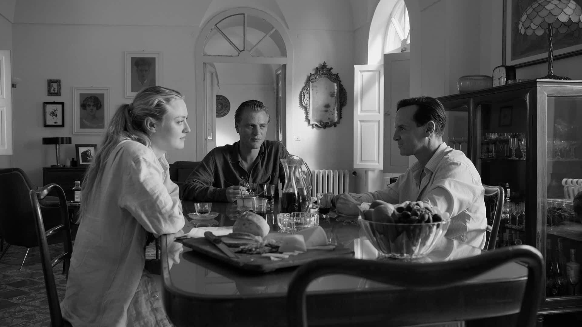 2WX4BKF-RM.jpg Black-and-white still from a movie scene where two men and a woman are sat a table together. The man and woman look suspiciously at the third man
