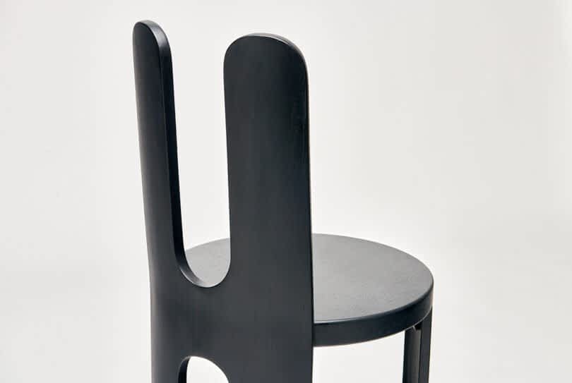Detail of a modern chair with a dark wood finish and a unique, dual backrest design.