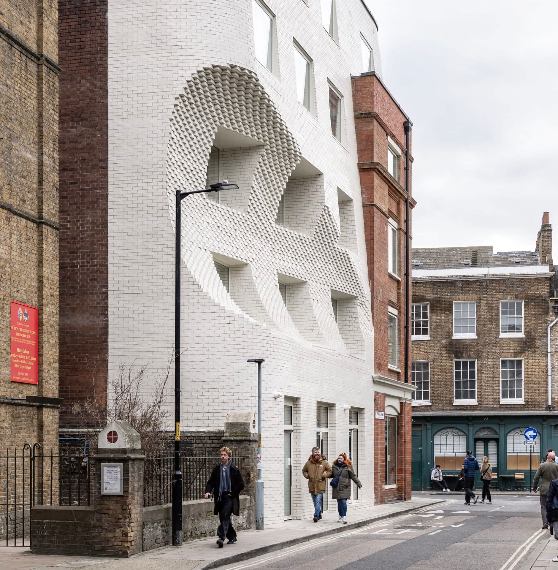 people walk by a white brick facade in London that looks like it has a large scoop carved out of it