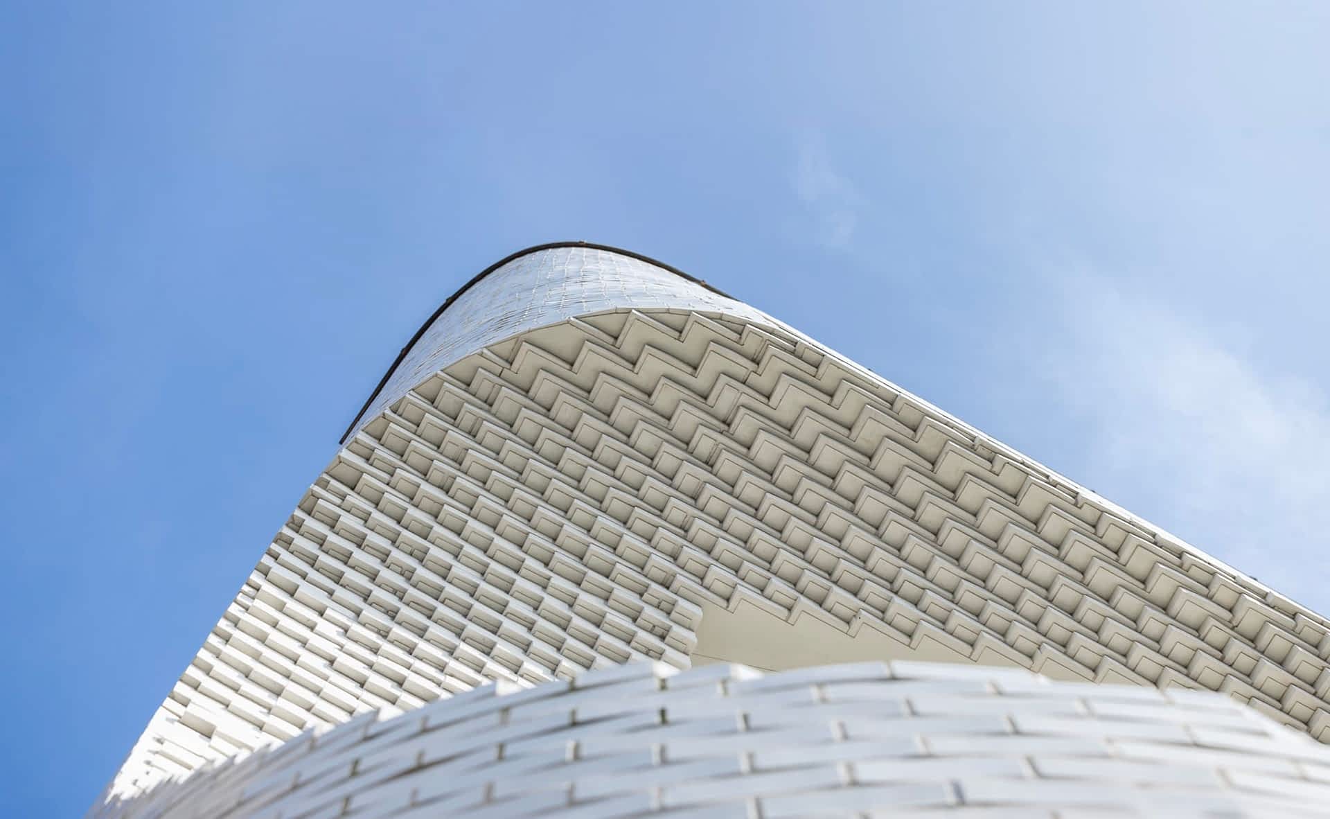 a detail of a white brick facade viewed from the ground, showing a concave form and numerous step-like patterns of bricks