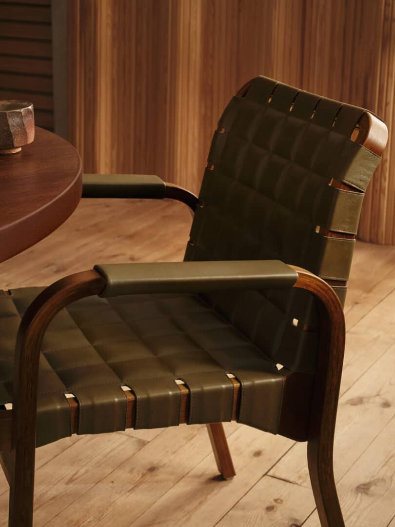 A wooden chair with green padded seat and backrest sits next to a round wooden table. The background includes wooden paneling and a wooden floor