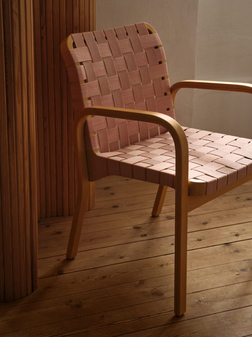 A wooden chair with a woven fabric seat and backrest is placed on a wooden floor next to vertical wooden slats