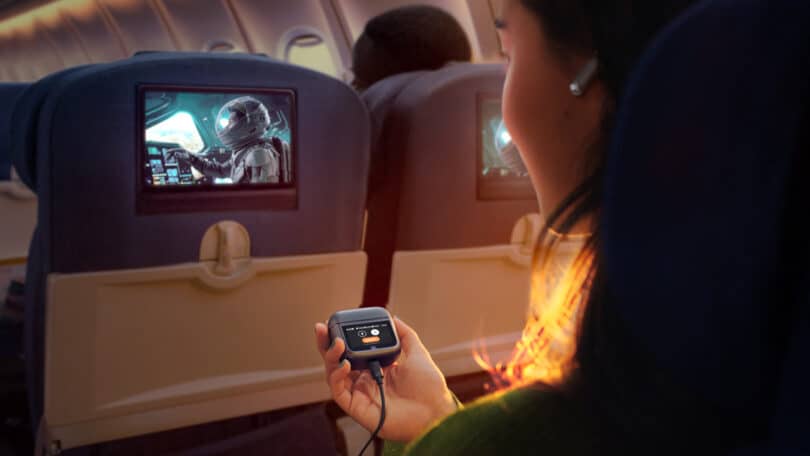A person on an airplane watching a sci-fi movie on the in-flight entertainment screen. The individual is holding a control device.