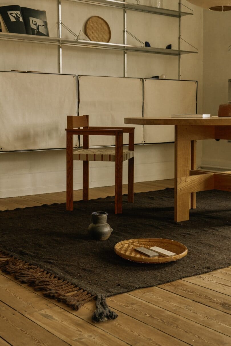 A minimalist interior featuring a dark-toned Beni rug with simple wooden furniture and a few curated objects