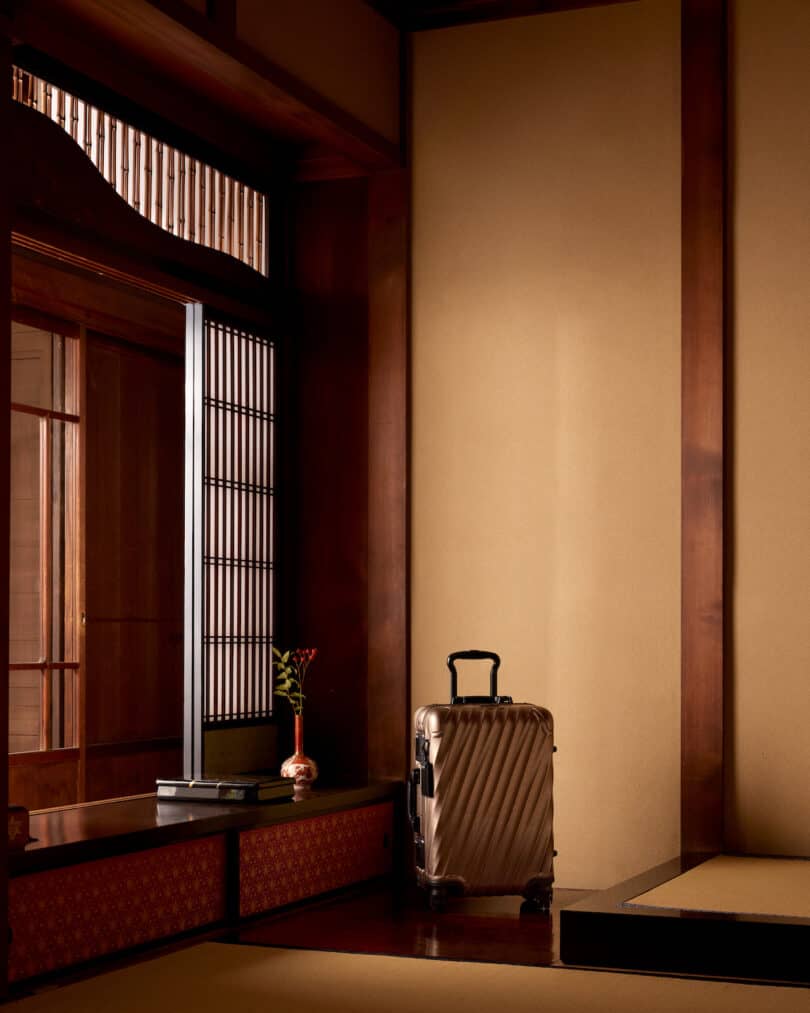 A silver suitcase with a textured design sits in a traditional Japanese room with wooden panels, shoji screens, and tatami mats