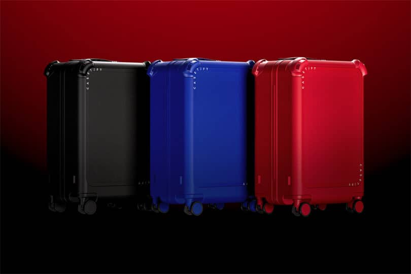 Three suitcases in black, blue, and red are standing upright against a gradient red to black background.