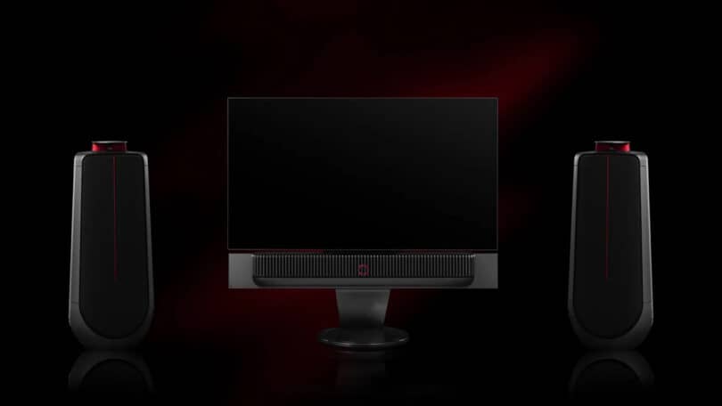 A sleek computer monitor with two tall, black speakers on each side, set against a dark background with a red accent.