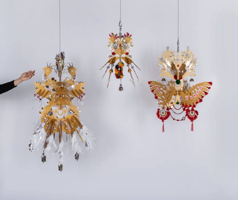 three abstract suspended yellow, white, and red sculptures with wing-like details