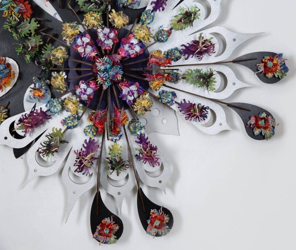 a detail of a sculptural wall piece made from mixed media, slightly resembling feathers that splay out from a central point