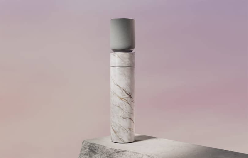 A cylindrical, marble-textured object with a small, gray speaker on top, placed on a stone surface against a gradient purple background.