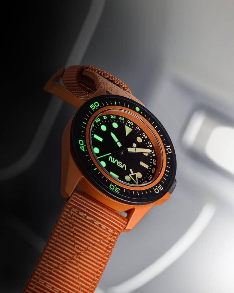 A watch with a brown strap and green glowing hands, featuring the NASA logo and a moon craters design on the black face.