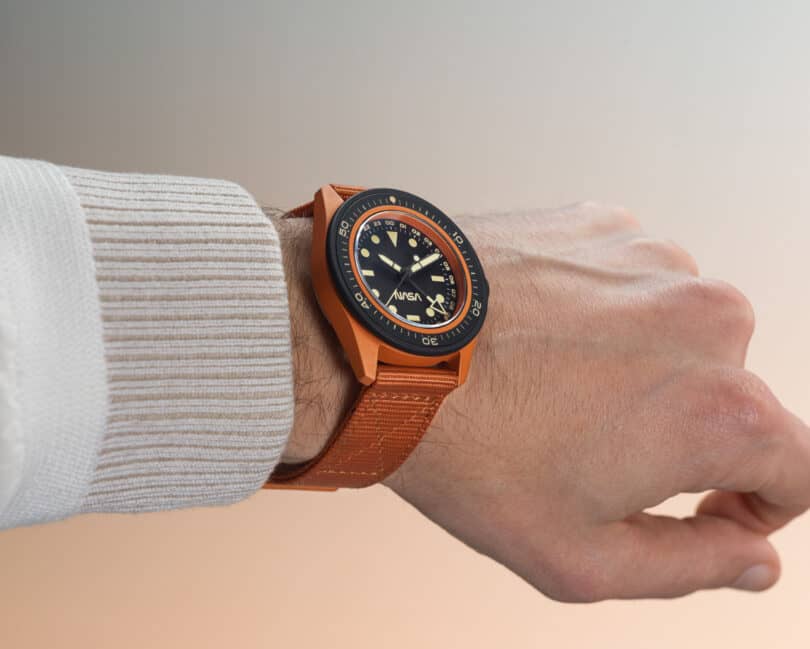 A person wearing a wristwatch with an orange strap and black dial, displaying the time on their left wrist.